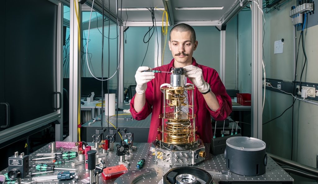 Ein KIT-Mitarbeiter integriert einen optischen Quantenspeicher in einen Kryostaten und koppelt ihn optisch per Glasfaser an ein supraleitendes Qubit